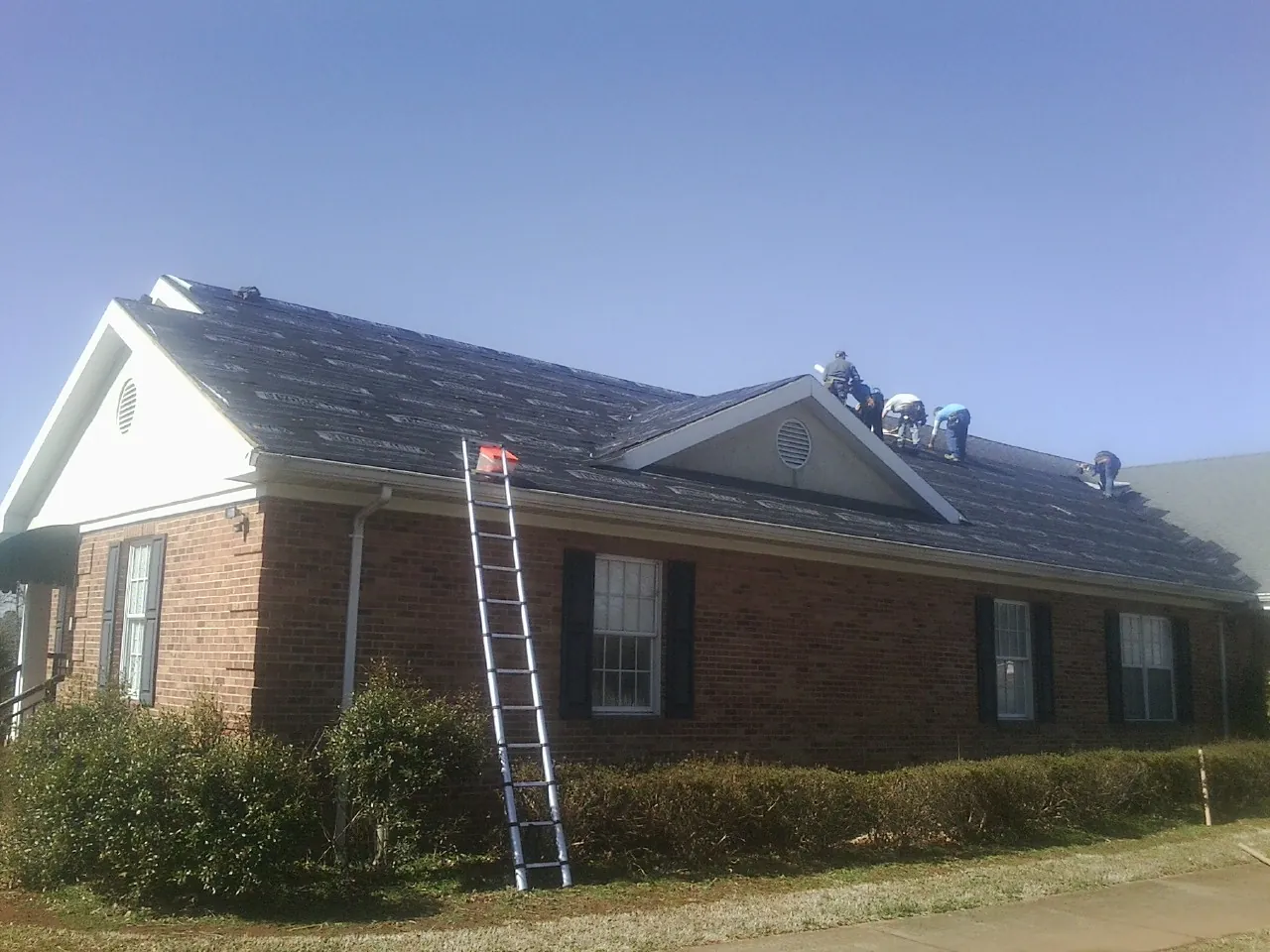 Crew tearing shingles off a brick ranch roof with a ladder set — Metal Roof Repair work by our crew in Graham